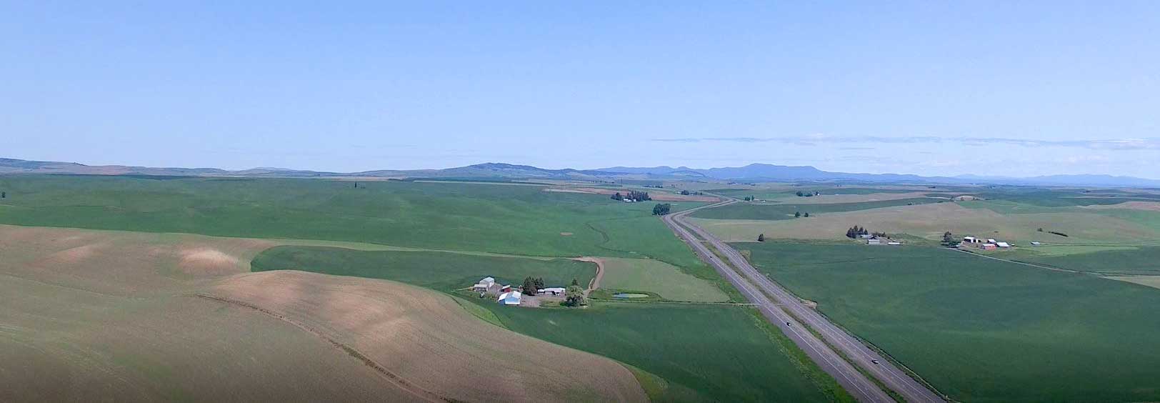 View of green rolling fields from overhead - highway going towards mountains in the distance